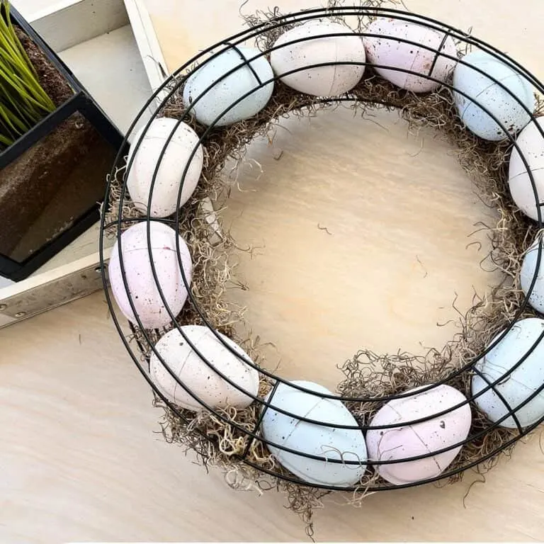 Photo of a finished Farmhouse Style Easter Egg wreath. The wreath uses two wire wreath forms, Spanish moss and feature pastel painted plastic eggs.