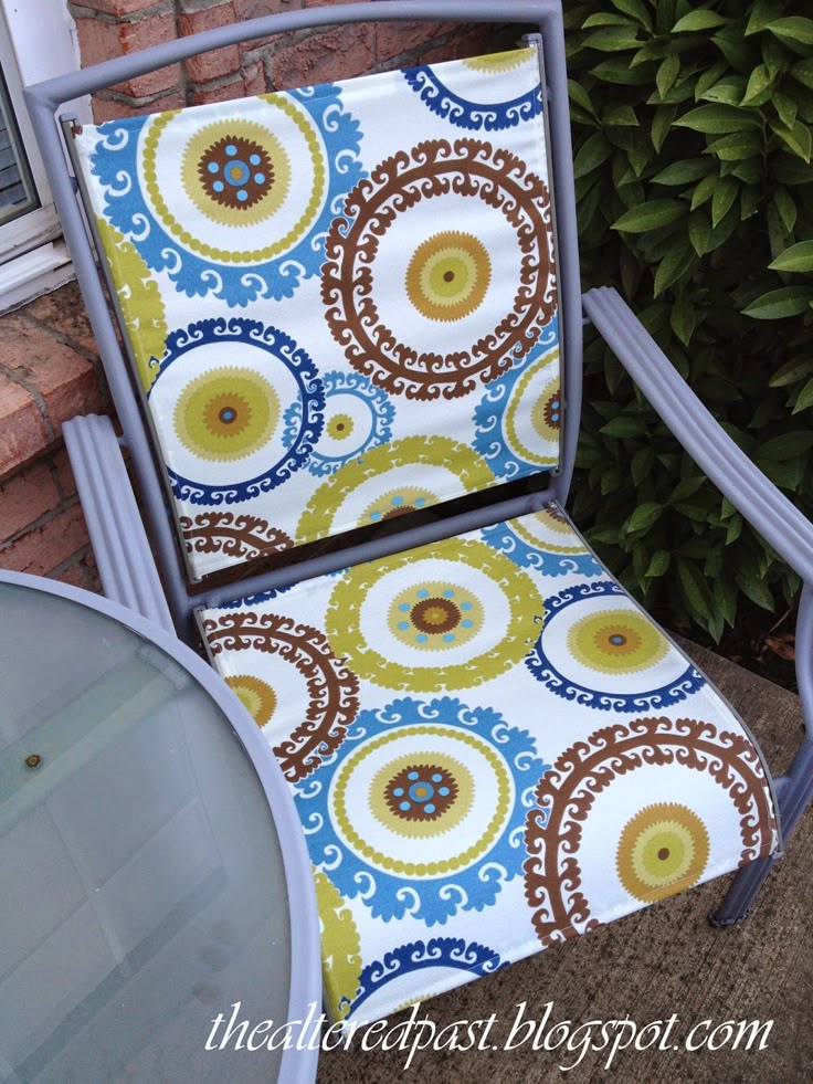 This may contain: a blue and yellow chair sitting on top of a brick patio next to a bush