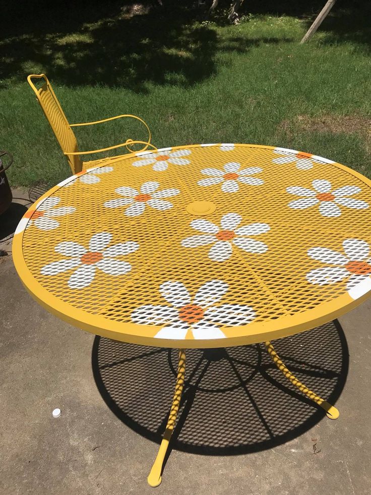 This may contain: a yellow table with white flowers painted on it and two chairs sitting in the background