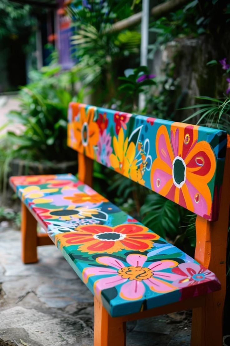 This may contain: a colorful painted bench sitting in the middle of some plants and flowers on it's sides